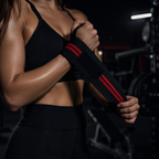 Athlete securing a black and red weightlifting wrist wrap with velcro closure and thumb loop in the gym